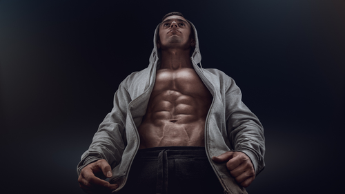 Bottom view of young strong bodybuilder showing off his physique against black background. Confident young fitness man with strong hands, abs and abdominal muscles best probiotic for men